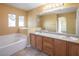 Bathroom featuring dual sinks, a soaking tub, and bright lighting at 7491 Speedwell Cavern St, Las Vegas, NV 89139