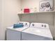 Bright laundry room features modern washer and dryer with storage shelf and humorous wall art at 48344 Orchid Ridge Ave # 104, Las Vegas, NV 89141