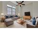 Staged living room with tile floors, two bright windows, ceiling fan, gray sofa and love seat and modern furnishings at 6844 Tropicaire St, Las Vegas, NV 89149
