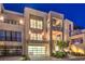 Evening view of a contemporary home featuring balconies, glass garage door, and manicured yard with lighting at 414 Tranquil Peak Ct, Henderson, NV 89012