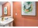 Stylish powder room with a pedestal sink, decorative mirror, and trendy artwork on a salmon colored wall at 6533 Cinnamon Hazelnut St # Lot 94, North Las Vegas, NV 89084
