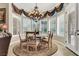 A sun-drenched dining area features elegant chandelier, bay window, and a circular rug under a round table at 1725 Cypress Manor Dr, Henderson, NV 89012