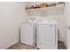 A simple laundry room is set up with modern, white, side-by-side washer and dryer and a shelf above at 6848 Sunflower Fields St, North Las Vegas, NV 89086