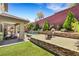 A spacious backyard featuring manicured lawn, stone patio, built in grill, and a covered seating area, perfect for outdoor entertaining at 10697 Acacia Park Pl, Las Vegas, NV 89135