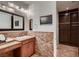 Well-lit bathroom featuring a TV, stone brick accent wall, sink, and dark wood cabinetry at 2435 Granada Bluff Ct, Las Vegas, NV 89135