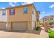 Two-story tan home with a two car garage, a red front door, and well manicured landscaping at 711 Florence Isle Ave, Henderson, NV 89015