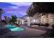 The backyard pool features uplighting, a covered patio area with an outdoor fireplace, lounge chairs, and tropical plants at 1610 Brock Ct, Las Vegas, NV 89117