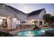 A backyard pool features lounge chairs, tropical plants, and uplighting illuminating a covered patio area at dusk at 1610 Brock Ct, Las Vegas, NV 89117