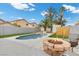 Serene backyard featuring a sparkling pool, desert trees, turf, and a stone fire pit with seating at 5937 Round Castle St, Las Vegas, NV 89130