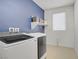 This spacious laundry room features a blue accent wall, shelving, and modern, front-loading washer and dryer at 9557 Belmont Bay Ave, Las Vegas, NV 89148