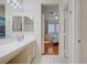 Bright bathroom showcasing a double sink vanity, large mirror with Hollywood lighting, and door to bedroom at 2325 Windmill Pkwy # 321, Henderson, NV 89074