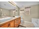 Bathroom featuring double sinks, wood cabinets, large mirror, tub, and tile flooring at 3232 Brayton Mist Dr, North Las Vegas, NV 89081