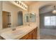 Well-lit bathroom with double sinks, large mirror, wood cabinets, and view to bedroom at 9994 Government Point Way # 101, Las Vegas, NV 89183