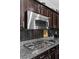 Close up of a gas cooktop, granite countertops, stainless steel microwave, and dark backsplash at 6857 Stone Tower Ct, Las Vegas, NV 89149