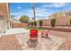 Spacious backyard with manicured bushes and artificial turf surrounding a gravel and paved seating area with red chairs at 3109 Siena Cir, Las Vegas, NV 89128