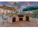 Stunning outdoor kitchen with stone counters, modern appliances, and shaded seating under a beautiful sunset at 6999 Stone Meadows Ave, Las Vegas, NV 89142