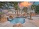Beautiful backyard pool area featuring a rock waterfall, hot tub, and lush palm trees against a colorful sky at 11158 Antonine Wall Ct, Las Vegas, NV 89141