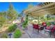 Beautiful outdoor patio with a stone fireplace, covered pergola, lush greenery, and comfortable seating area at 1432 Castle Crest Dr, Las Vegas, NV 89117