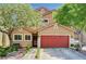 Inviting two-story home featuring a red garage door and well-maintained landscaping with flowering trees at 9370 Corkfish St, Las Vegas, NV 89178