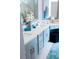 Bright bathroom with dual sinks, white countertops, light grey cabinetry, and a dark ottoman at 7607 Boca Raton Dr, Las Vegas, NV 89113