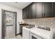 Modern laundry room boasts black cabinets, gold hardware, striking backsplash, sink and white washer and dryer at 9029 Rivers Edge Dr, Las Vegas, NV 89117