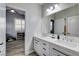 Bright bathroom featuring double sinks, white cabinets, and modern fixtures; a view into the adjacent bedroom at 9349 Olympia Falls Ave, Las Vegas, NV 89149