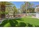 Serene backyard with a custom rock feature, green lawn, and mature trees, perfect for outdoor enjoyment at 2231 S Tioga Way, Las Vegas, NV 89117