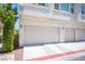 Three-car garage featuring tan doors, and exterior wall lighting with exterior landscaping at 9322 Straw Hays St # 103, Las Vegas, NV 89178