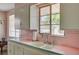 Close up of the kitchen sink, featuring a double basin sink, pastel pink countertops, and a large window at 557 6Th St, Boulder City, NV 89005