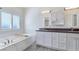 Bright bathroom with white cabinets, dual sinks, soaking tub, and window at 5500 Santovito St, Pahrump, NV 89061