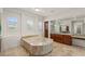 Bathroom with marble counters, wood cabinetry, and sunken tub with travertine surround at 2436 Grassy Spring Pl, Las Vegas, NV 89135