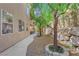 A tranquil backyard featuring gravel, trees, and a cozy patio beneath a balcony, enhanced by a stone retaining wall at 6739 Quapaw St, Las Vegas, NV 89149