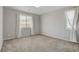 This bright bedroom features neutral walls, plush carpet, and two large windows dressed with long, elegant white curtains at 10433 Ember Rose Ave, Las Vegas, NV 89135