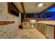 Covered outdoor kitchen features stone accents, built-in grill, bar seating, TV, and mini fridge, perfect for gatherings at 10433 Ember Rose Ave, Las Vegas, NV 89135