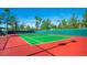 Single tennis court surrounded by lush greenery, under a bright blue sky with a covered bench on the side at 2816 High Range Dr, Las Vegas, NV 89134