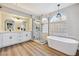 Bright bathroom featuring a soaking tub, walk-in shower, and dual sink vanity with stylish fixtures and wood-look flooring at 2409 Alpine Meadows Ave, Henderson, NV 89074