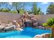 Lagoon style pool with rock waterfall, surrounded by desert landscaping and mature trees at 2409 Alpine Meadows Ave, Henderson, NV 89074