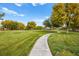 Serene view of a neighborhood park with a winding path, green lawns, and mature trees under a clear blue sky at 7119 Wolf Rivers Ave, Las Vegas, NV 89131