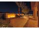Inviting backyard featuring a brick fireplace and pavers, complemented by lush landscaping and palm trees at night at 6110 Pebble Glen Ct, Las Vegas, NV 89149