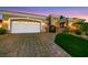 Elegant single-story home featuring a brick driveway, attached garage, and manicured landscaping at dusk at 4286 Pacifico Ln, Las Vegas, NV 89135