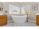 Bright bathroom featuring a standalone tub with modern fixtures under two large windows and wooden cabinets with white countertops at 7411 Brittlethorne Ave, Las Vegas, NV 89131
