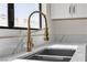 Close-up of a stylish kitchen sink with a modern gold faucet and white marble countertops by a window at 6204 Robin Hood Cir, Las Vegas, NV 89108