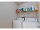 Bright laundry room featuring a white washer and dryer, a shelf with cleaning supplies, and white walls at 9039 Alex Creek Ave, Las Vegas, NV 89149