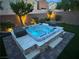 Modern hot tub with tiered platform, illuminated at night, amidst landscaping and exterior stone wall at 7424 Rainford St, Las Vegas, NV 89148