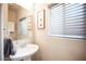 Chic powder room with a pedestal sink, decorative mirror, and stylish window blinds at 9807 Panther Hollow St, Las Vegas, NV 89141