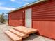 Exterior view of the red cabin entry has a white door, wood steps, and desert landscape at 70 Camp Bonanza Rd, Las Vegas, NV 89124