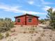 Exterior view of the red cabin shows the front entry, windows, and surrounding desert landscape at 70 Camp Bonanza Rd, Las Vegas, NV 89124