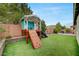 Landscaped backyard with artificial grass, a playhouse with a climbing wall and slide, and a seating area at 2433 Amatrice St, Henderson, NV 89044