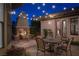 Warm outdoor patio with dining set, stone fireplace, string lights, and manicured landscaping for relaxing evenings at 64 Tapadero Ln, Las Vegas, NV 89135
