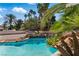 Beautiful pool area featuring a built-in waterfall, rocks, and lush tropical landscaping with palm trees at 13 Dovetail Cir, Henderson, NV 89014